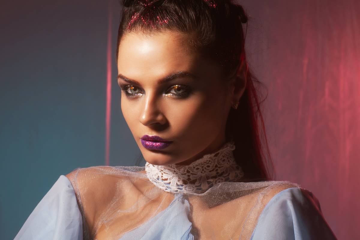 Model showcasing chic makeup style with dewy skin, soft smoky eyes, and bold lip on red carpet backdrop